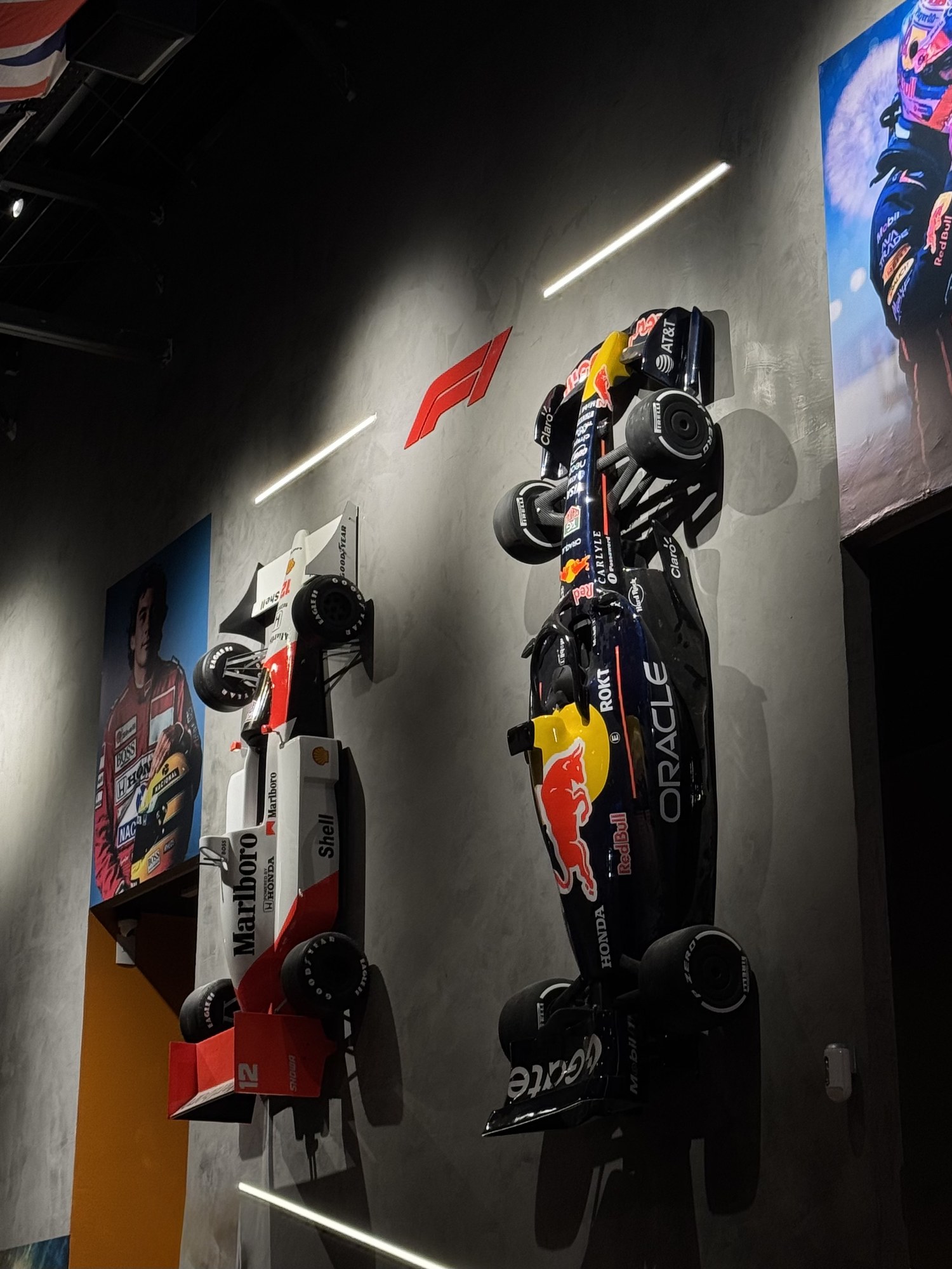 Réplicas em escala dos carros de F1 de Senna e Verstappen na parede do Olimpia